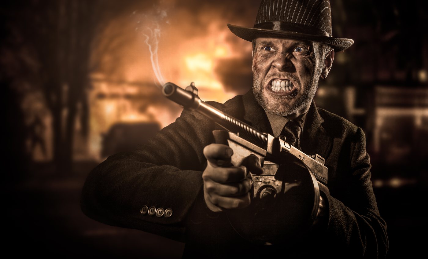 Homme en costume et chapeau devant une maison en flammes